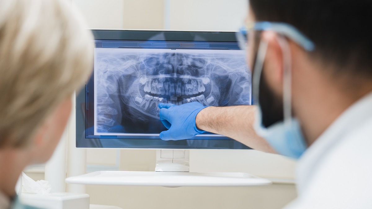 Back view shot of male dentist orthodontist showing explaining an x-ray photo of jaws on computer screen to a female patient in dental clinic